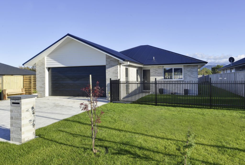The frontage of a freshly built modern home with a garage, letterbox, steel fence and young maple tree