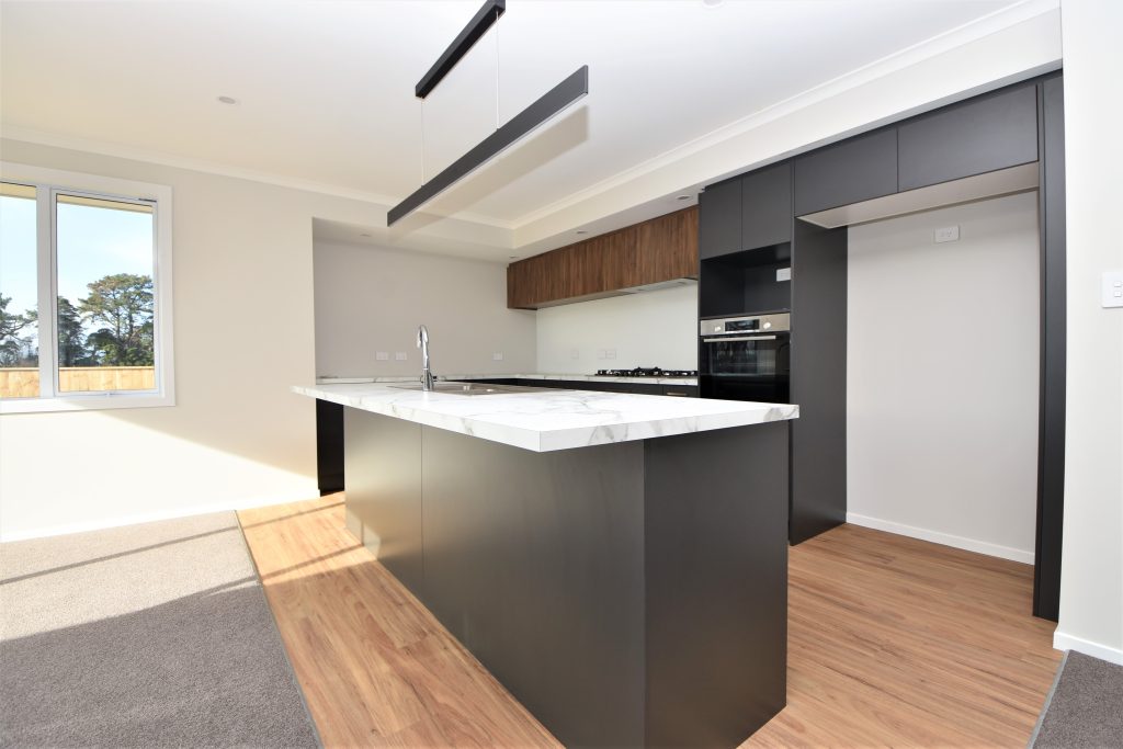 A freshly built and empty open-plan kitchen with white marble bench top and dark cupboards