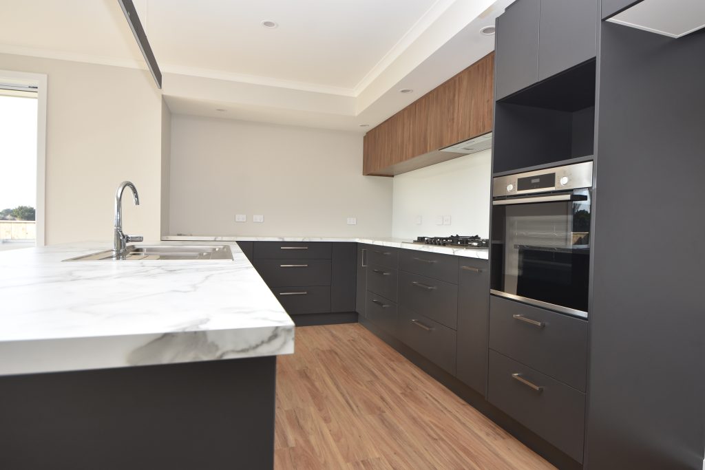 A freshly built and empty open-plan kitchen with white marble bench top and dark cupboards