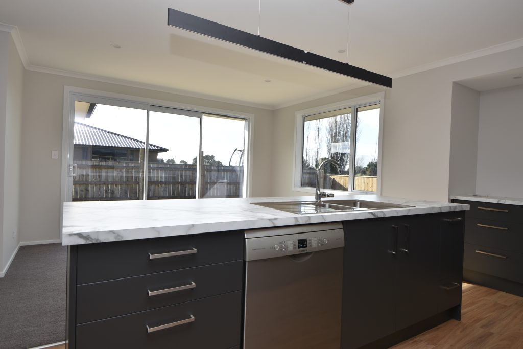 A freshly built and empty open-plan kitchen with white marble bench top and dark cupboards