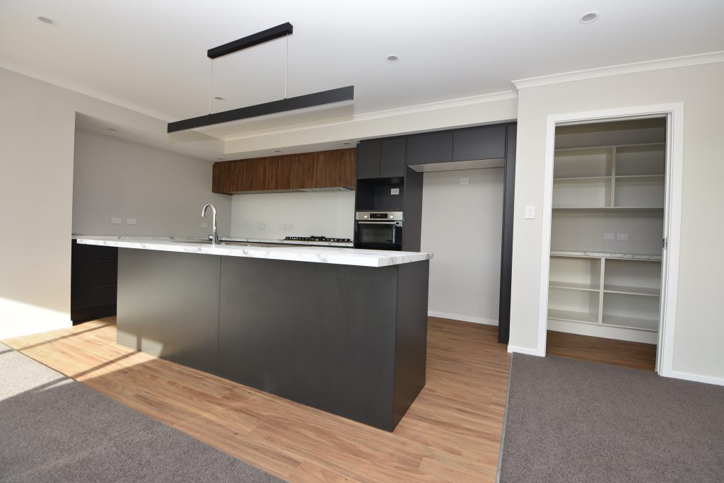 A freshly built and empty open-plan kitchen with white marble bench top and dark cupboards