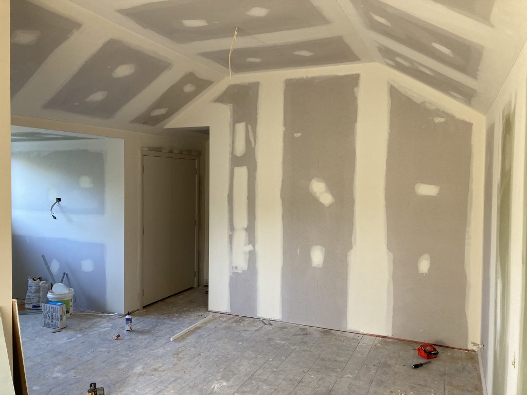 The inside of a house undergoing a renovation showing exposed completed gib / drywall, plastered and ready for painting with various builders tools on the floor.
