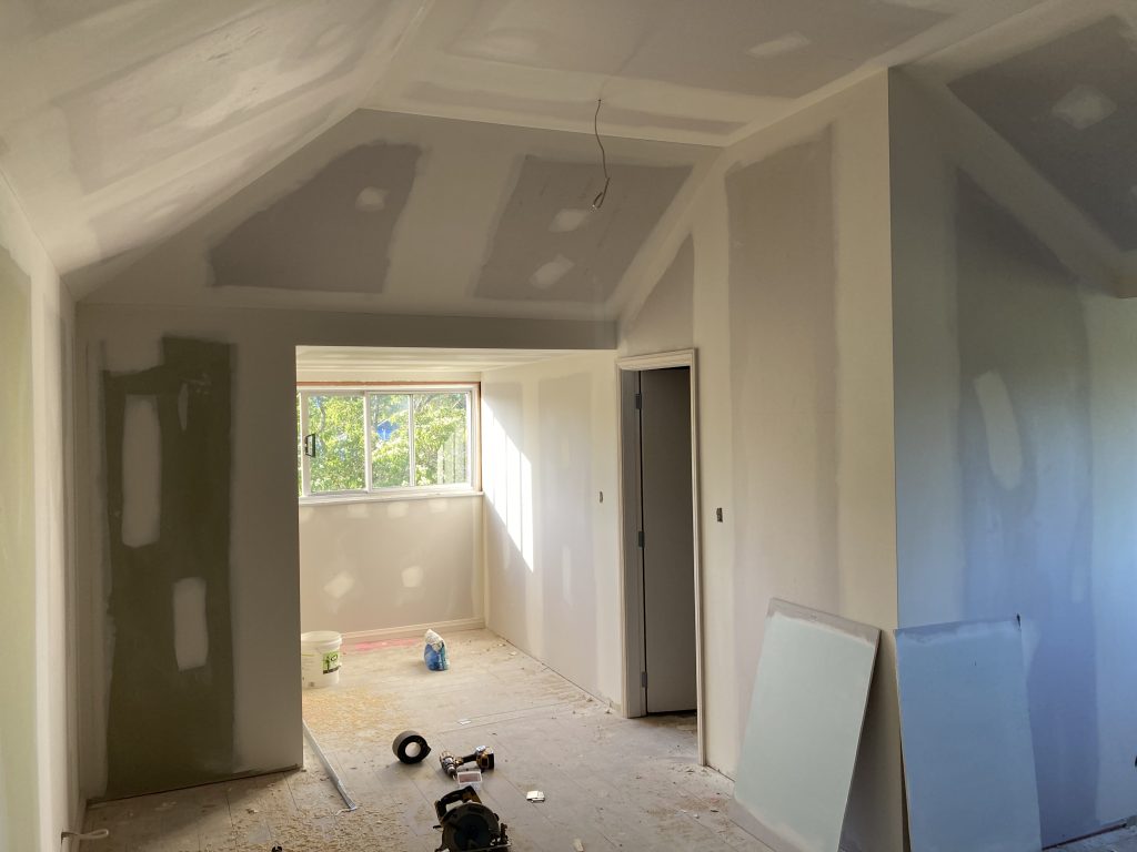The inside of a house undergoing a renovation showing exposed completed gib / drywall, plastered and ready for painting with various builders tools on the floor.